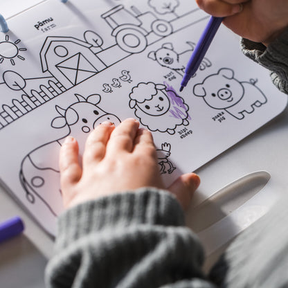 A child coloring a black-and-white farm animal activity sheet with a purple marker, shown from an overhead angle at a table.