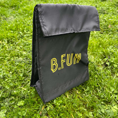 Insulated lunch carry bag in black with yellow text saying B.FUN sitting on green grass.