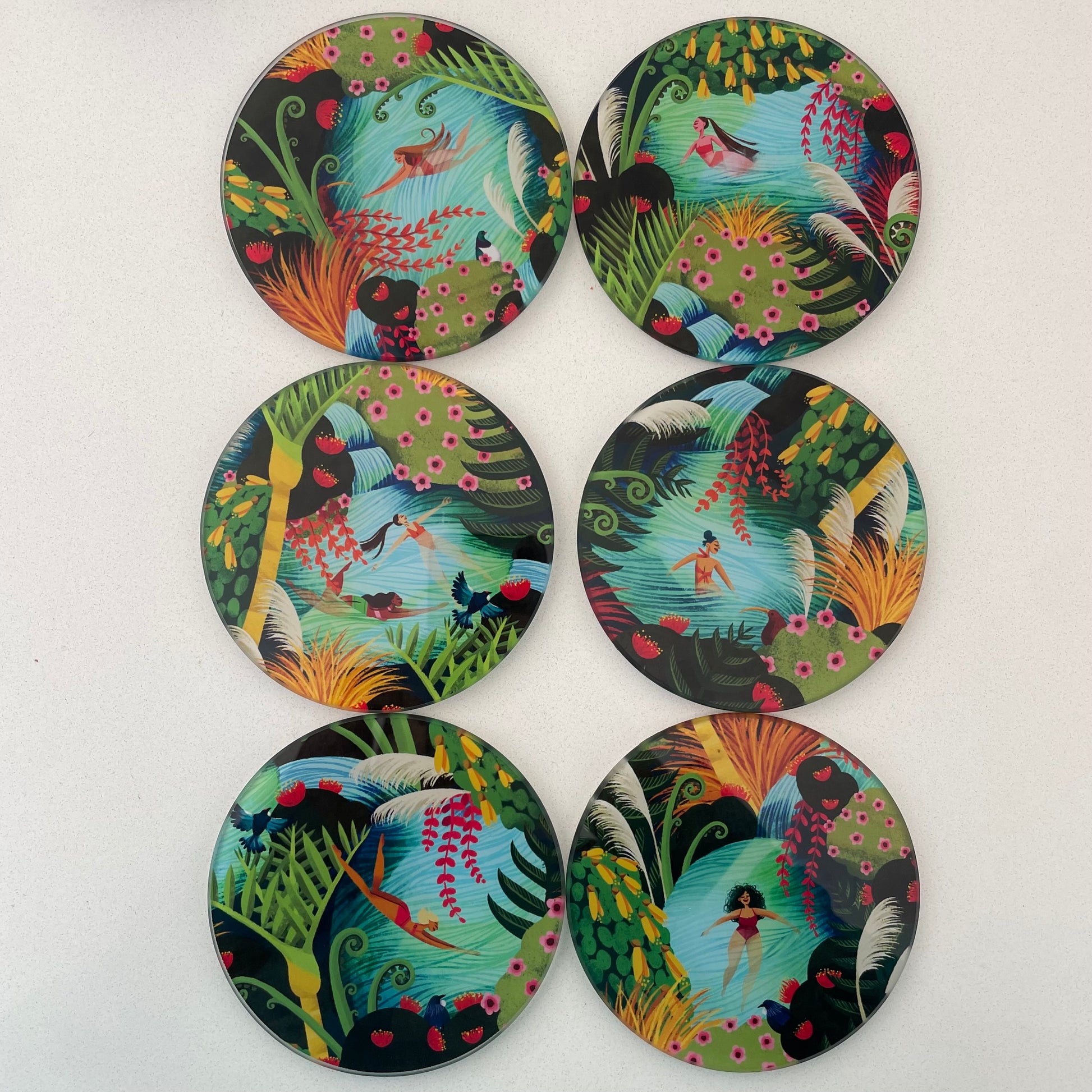 Set of 6 round glass coasters featuring bright colourful artwork of native New Zealand flora & fauna and women swimming in water. Each one is a different image.