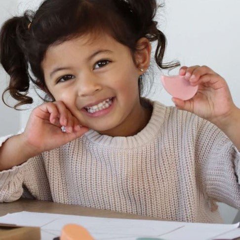 Young girl holding a pink petal shaped crayon.