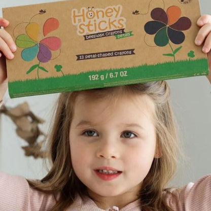 Youn girl holding a cardboard box of Honeysticks petal shaped crayons above her head.