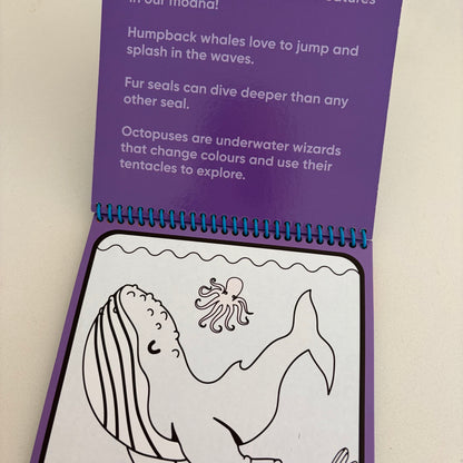 A children's spiral-bound booklet or activity book shown open on a light beige surface. The page has a purple header with printed text about whales, seals, and octopuses, and a white lower panel with black line drawings of a whale and octopus.