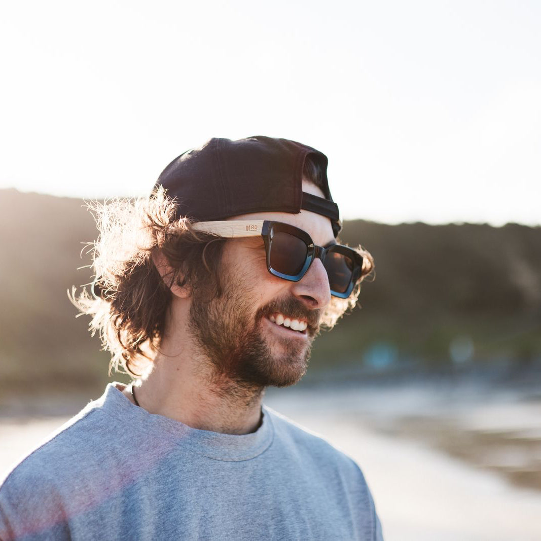 Man wearing sunglasses and a cap by a body of water with mountains in the background