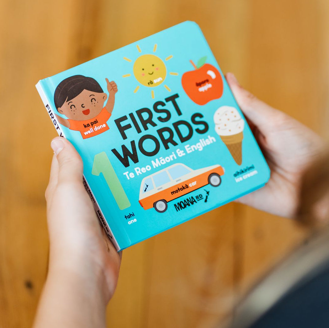 Children's book titled 'First Words' held by a person against a wooden background
