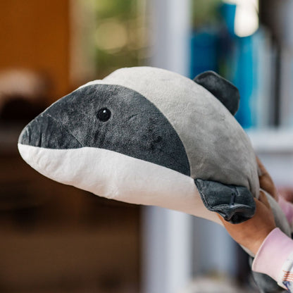 A plush Hectors Dolphin toy being held by a childs hands against a blurred background.