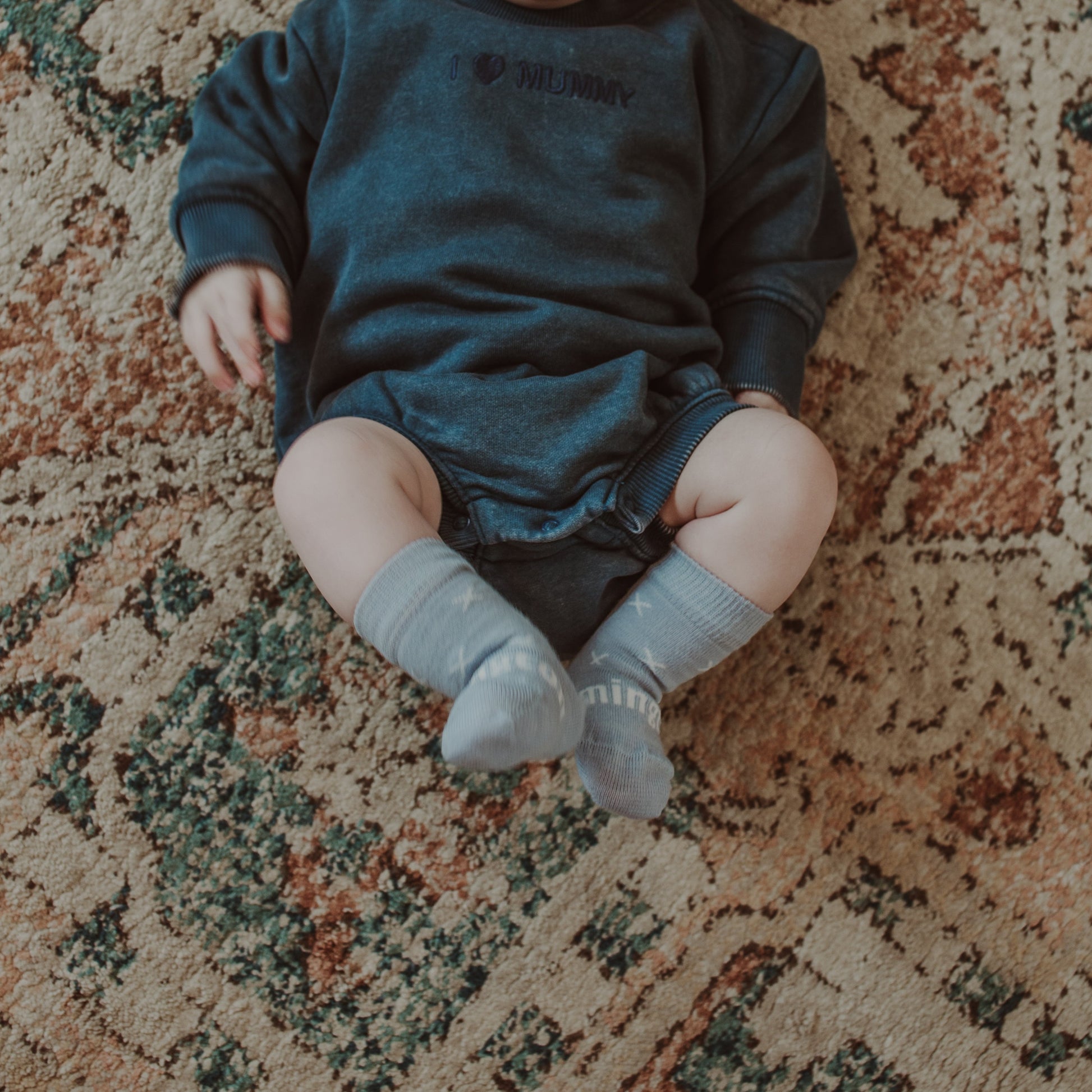 Baby lying on a mat wearing crew socks in pale blue knit merino wool with a white X pattern.