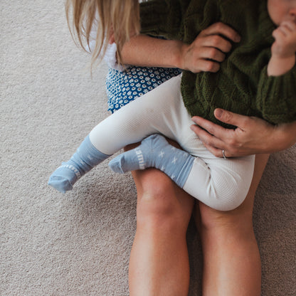Women holding a baby who is wearing white leggings and Baby crew socks in pale blue knit merino wool with a white X pattern.