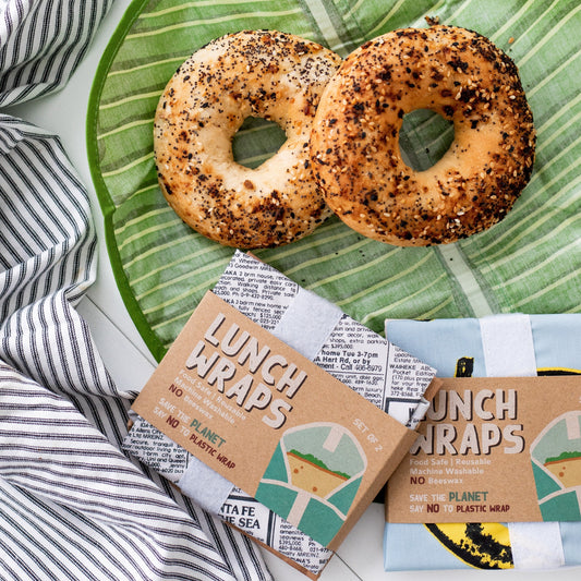 Two bagels sitting on a leafy print lunch wrap and 2 packages of more lunch wraps on the side.