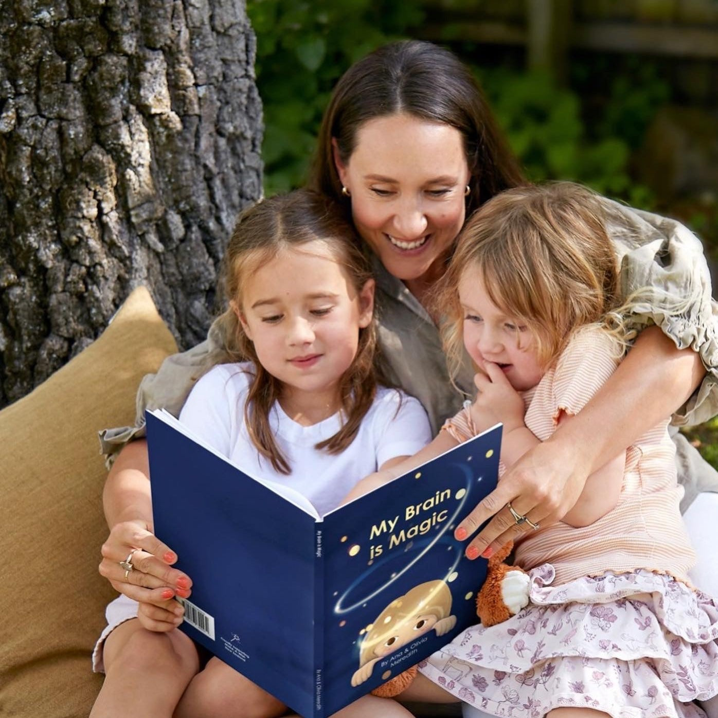 Woman reading a book called "My Brain is Magic" to two children.