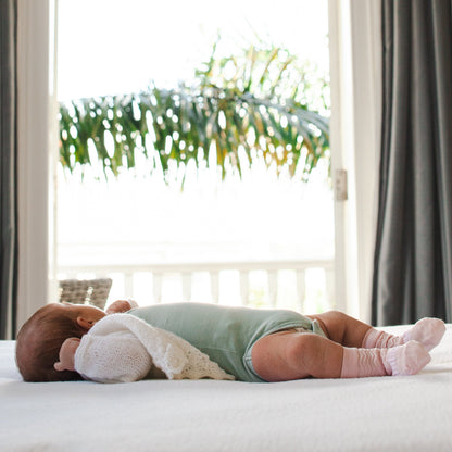 Baby lying on its back on a bed looking out a window wearing pink merino socks.
