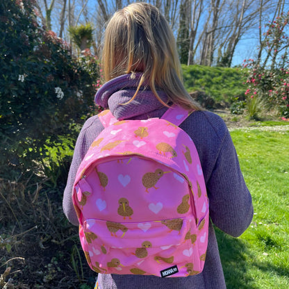 Child wearing a pink backpack with hearts and kiwi bird prints.