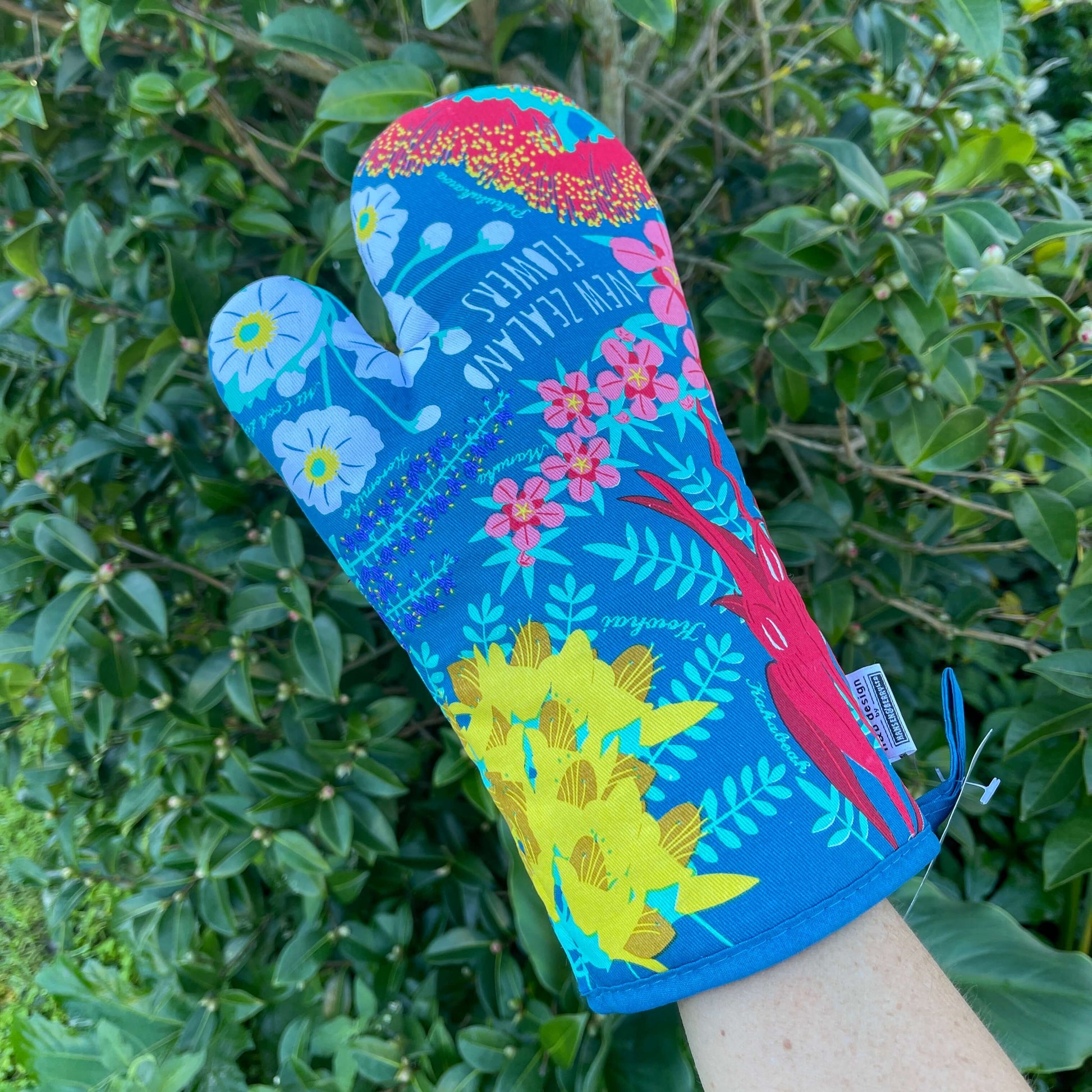 Dark teal blue oven mitt with bright NZ flowers printed on it.