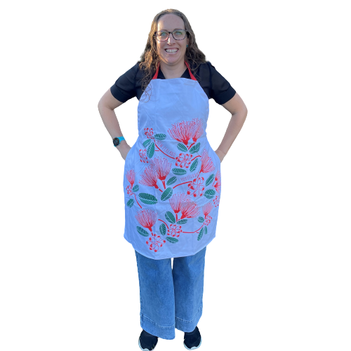 Women wearing a white apron with red and green pohutukawa flower print.