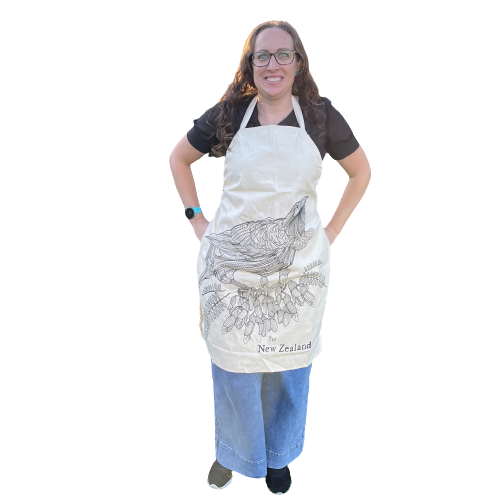 Woman wearing calico apron with black sketch of a Tui bird and kowhai flowers.