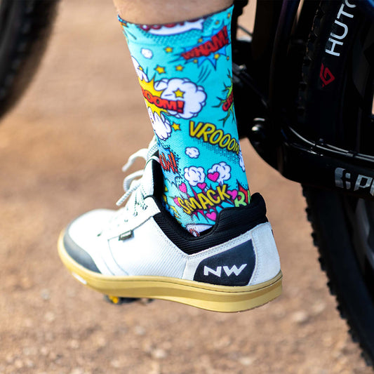 Foot wearing white and black shoes on bike pedal with mutli-coloured bright comic style socks socks