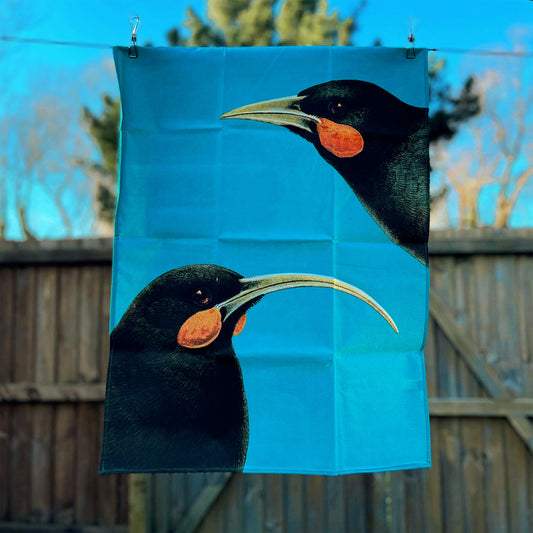 Bright blue tea towel with 2 Huia birds on it.