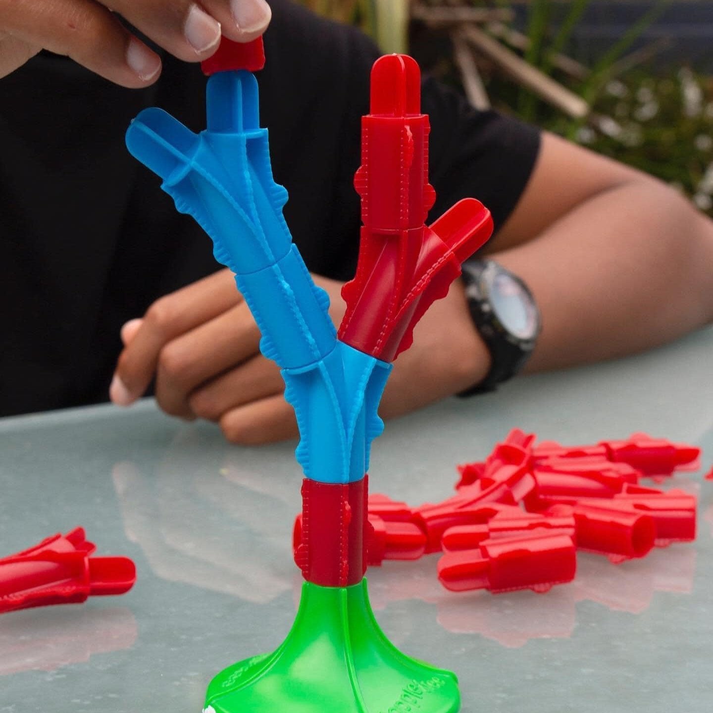 Childs hand placing a new branch block onto an existing piece of a Toppletree game.