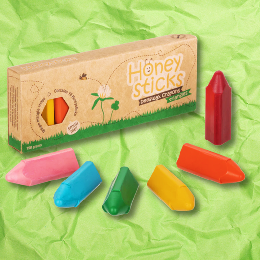 Honeysticks Triangle Beeswax crayon box with multi-coloured crayons arranged in front on a green crumpled paper background