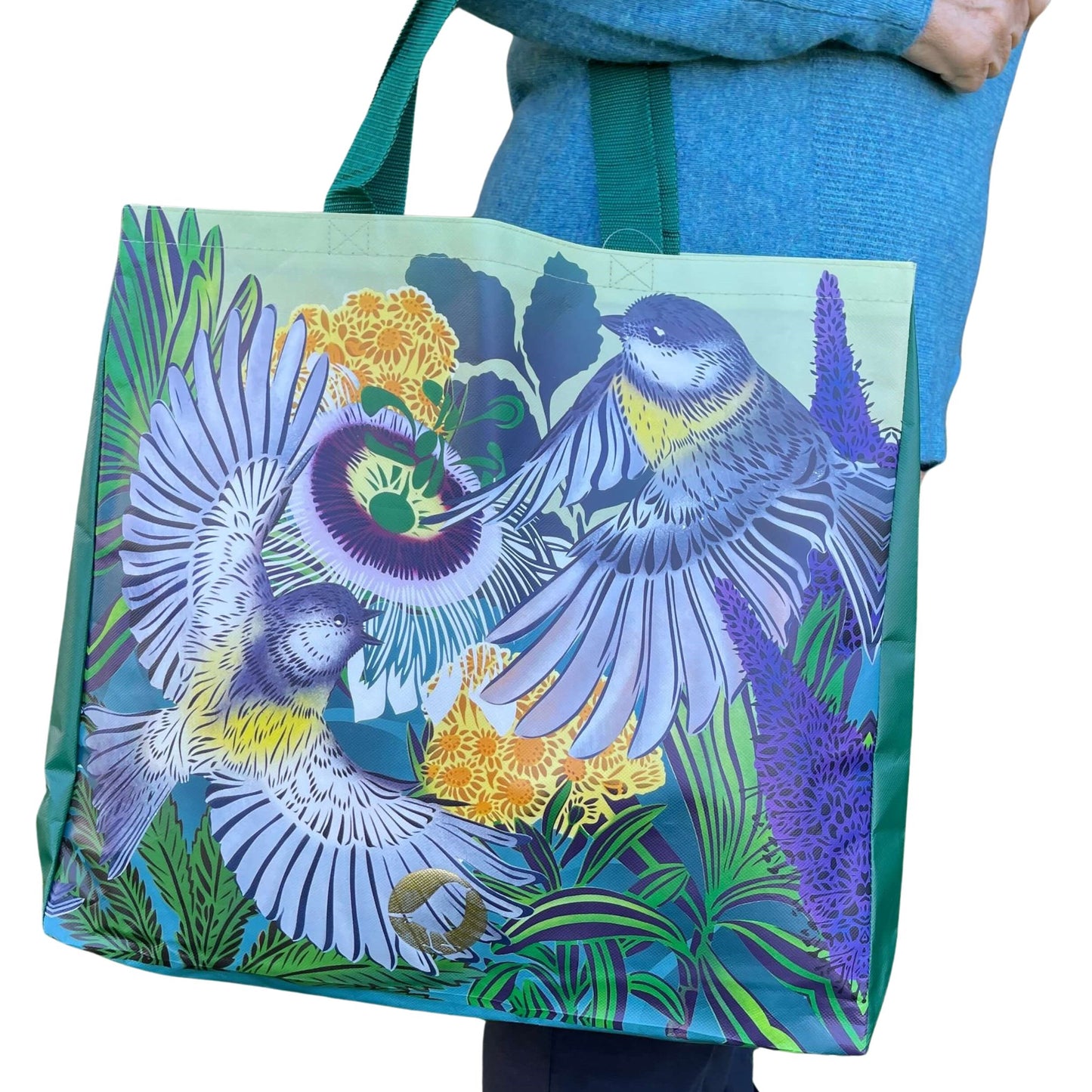 Woman with a tote bag over her arm. The vibrant coloured tote bag features Miromiro birds by artist Flox.