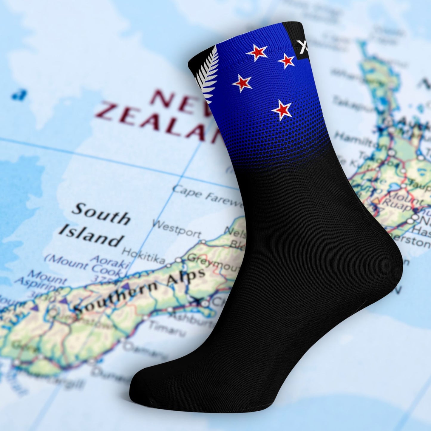 New Zealand Silver Fern design sock. Black socks with blue bank on top featuring the southern cross and the silver fern icon. The background is of a NZ map