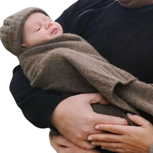 Baby in parents arms wrapped in a brown woolen blanket and wearing a matching hat.