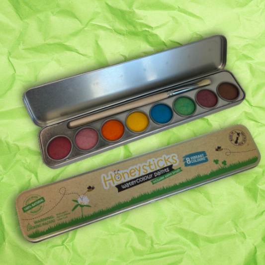 Watercolour paints in a tin. One tin is closed and one tin is open revealing the bright multicoloured paints and the paint brush inside.