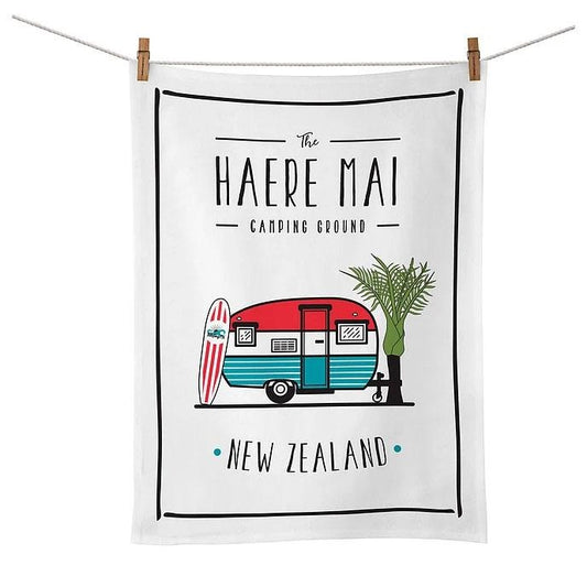White tea towel with caravan, surfboard and palm tree. Words say The Haere Mai Camping Ground, New Zealand.