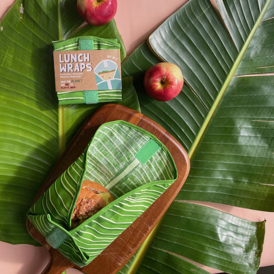 Lunch wraps in a leaf pattern sitting on top of large leaves with some apples.