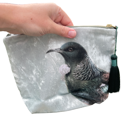 Velvet cosmetic bag featuring the head of a Tui bird held in a persons hand.