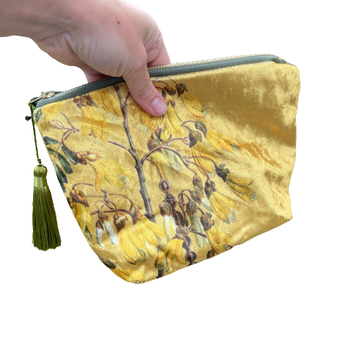 Golden velvet cosmetic bag with Kowhai flowers on it being held in a hand.