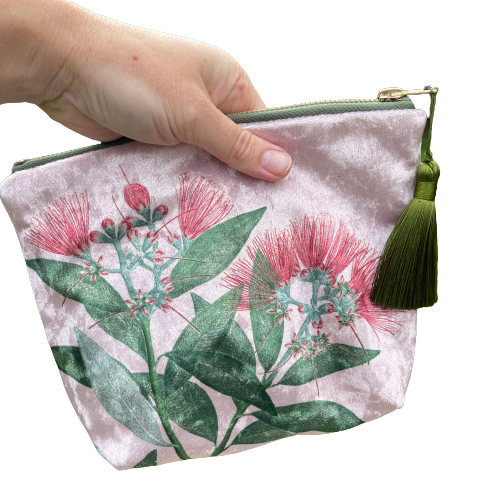 Pale pink velvet cosmetic bag with green tassel and a pohutukawa flower print being held by a person.
