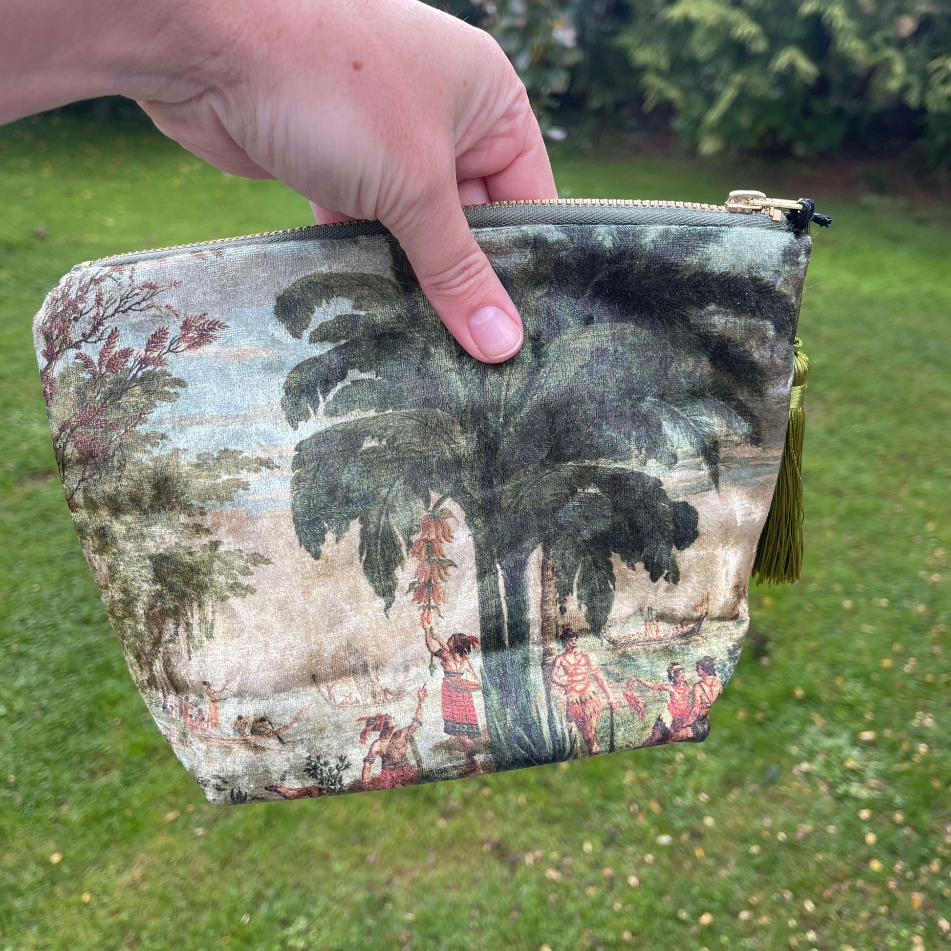 Persons hand holding a velvet cosmetic bag featuring a scene from a Joseph Dufour painting.