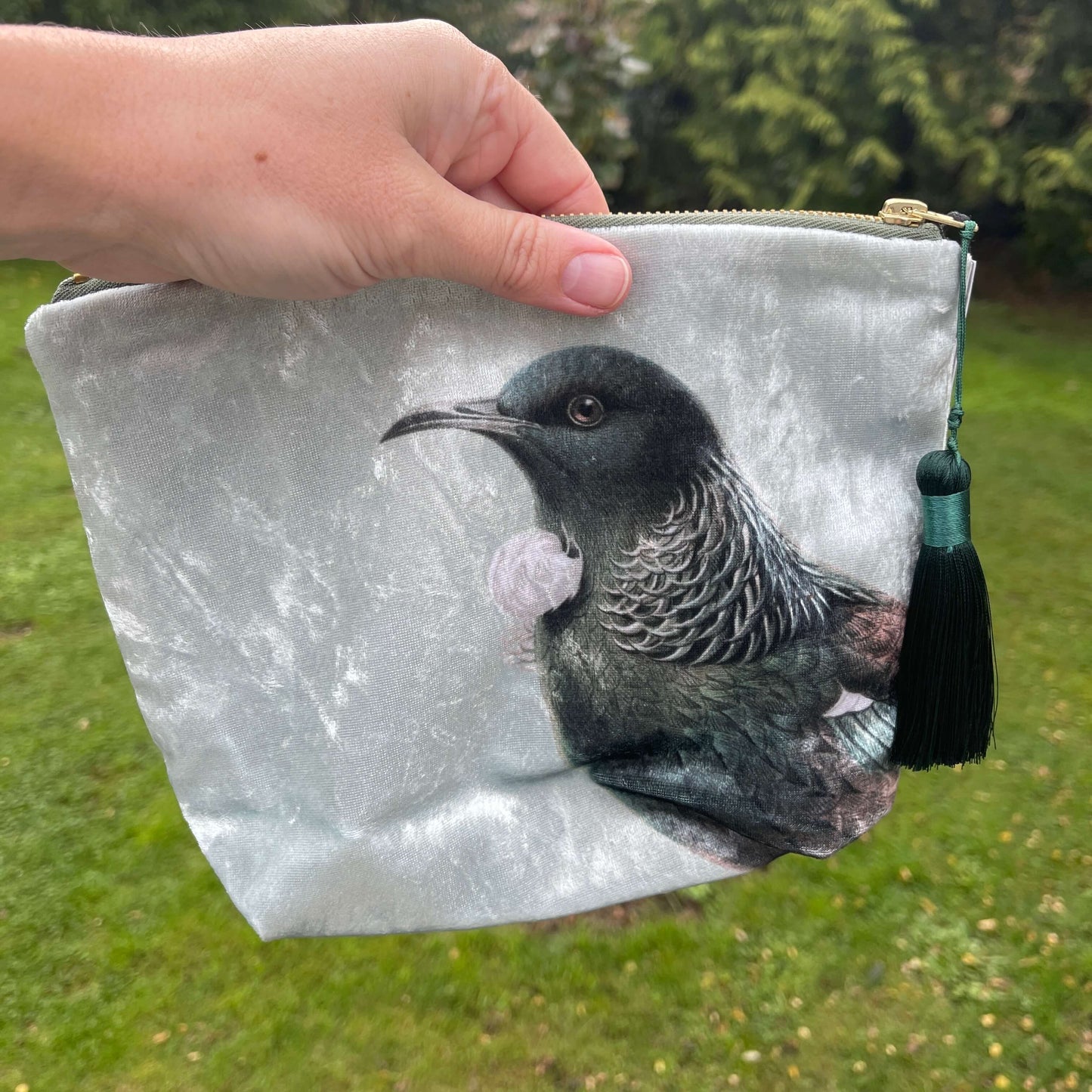 Velvet cosmetic bag featuring the head of a Tui bird being held by a persons hand.