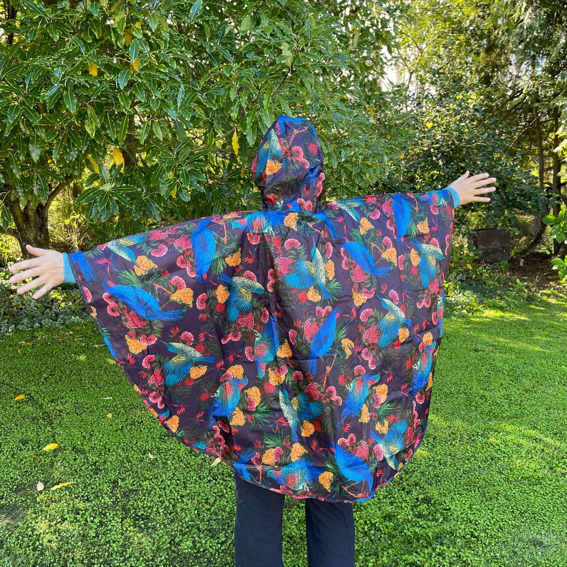 Woman wearing a rain poncho with birds and flower print on a deep aubergine purple background.