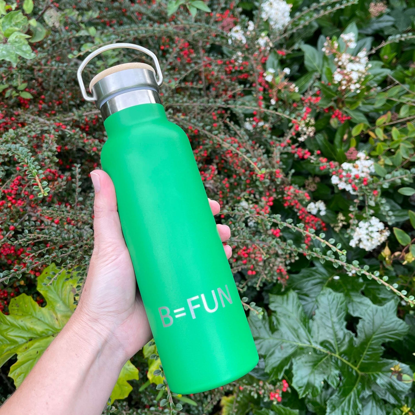 Womens hand holding a bright green stainless drink bottle with a bamboo cap and the words B=FUN engraved on it.