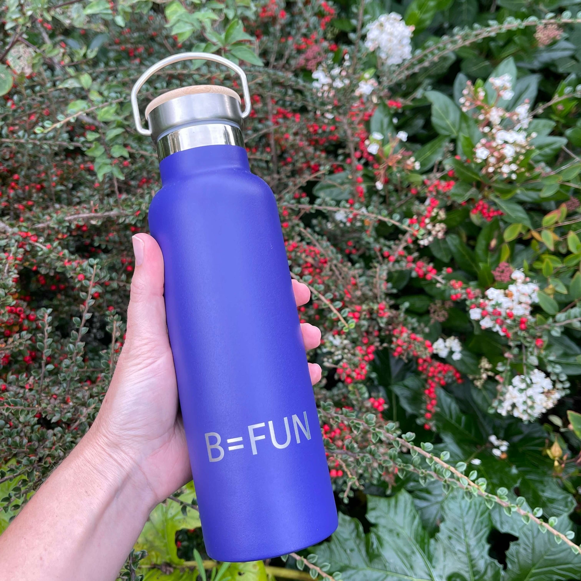 Womens hand holding a dark blue stainless drink bottle with a bamboo cap and the words B=FUN engraved on it.