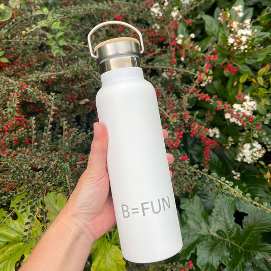 Womens hand holding a snowy white stainless drink bottle with a bamboo cap and the words B=FUN engraved on it.