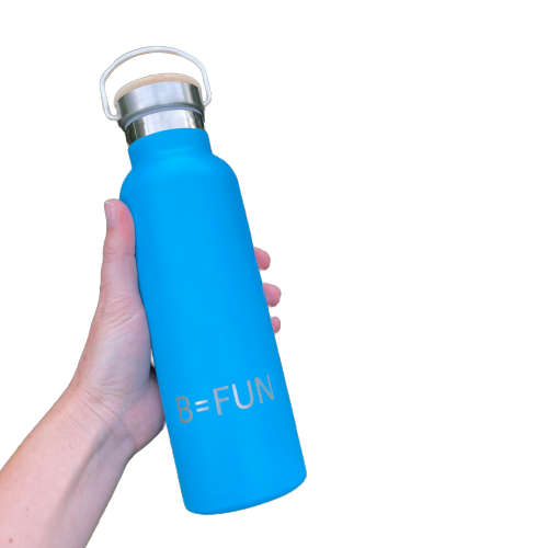 Womens hand holding a bright blue stainless drink bottle with a bamboo cap and the words B=FUN engraved on it.