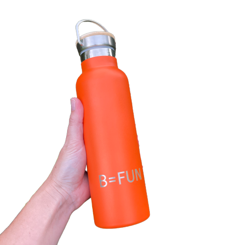 Womens hand holding a bright orange stainless drink bottle with a bamboo cap and the words B=FUN engraved on it.