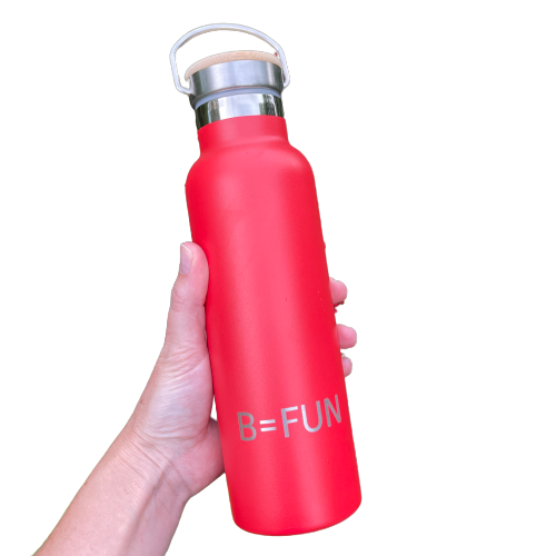 Womens hand holding a bright red stainless drink bottle with a bamboo cap and the words B=FUN engraved on it.