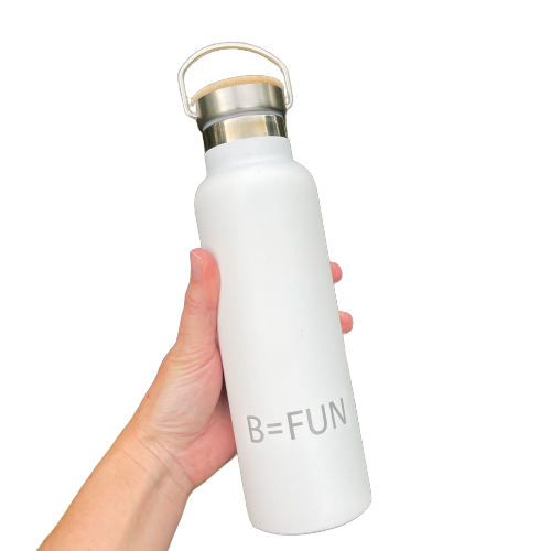 Womens hand holding a snowy white stainless drink bottle with a bamboo cap and the words B=FUN engraved on it.
