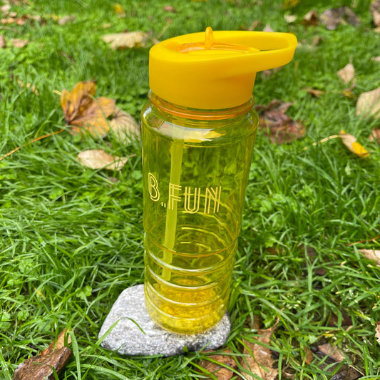 Bright yellow plastic sports water bottle with B=Fun printed on it sitting on a rock in the grass.