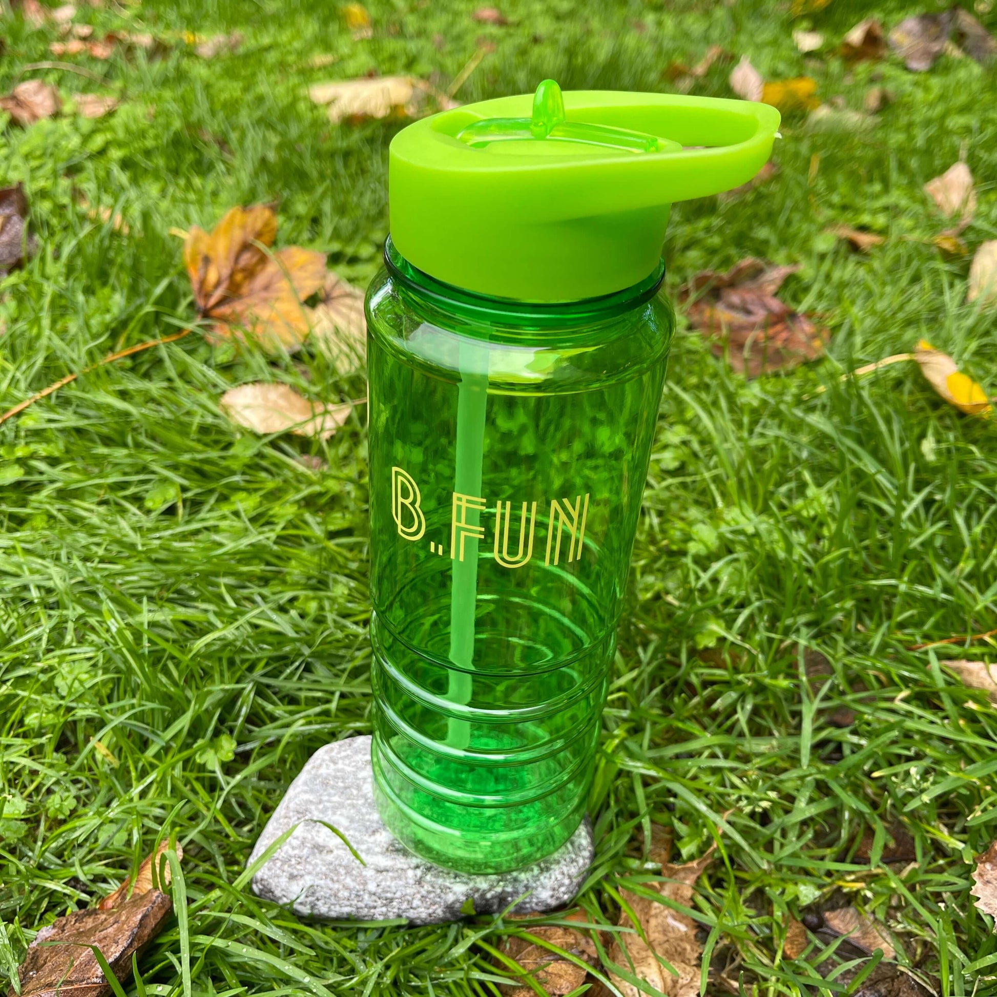 Bright green plastic sports water bottle with B=Fun printed on it sitting on a rock in the grass.