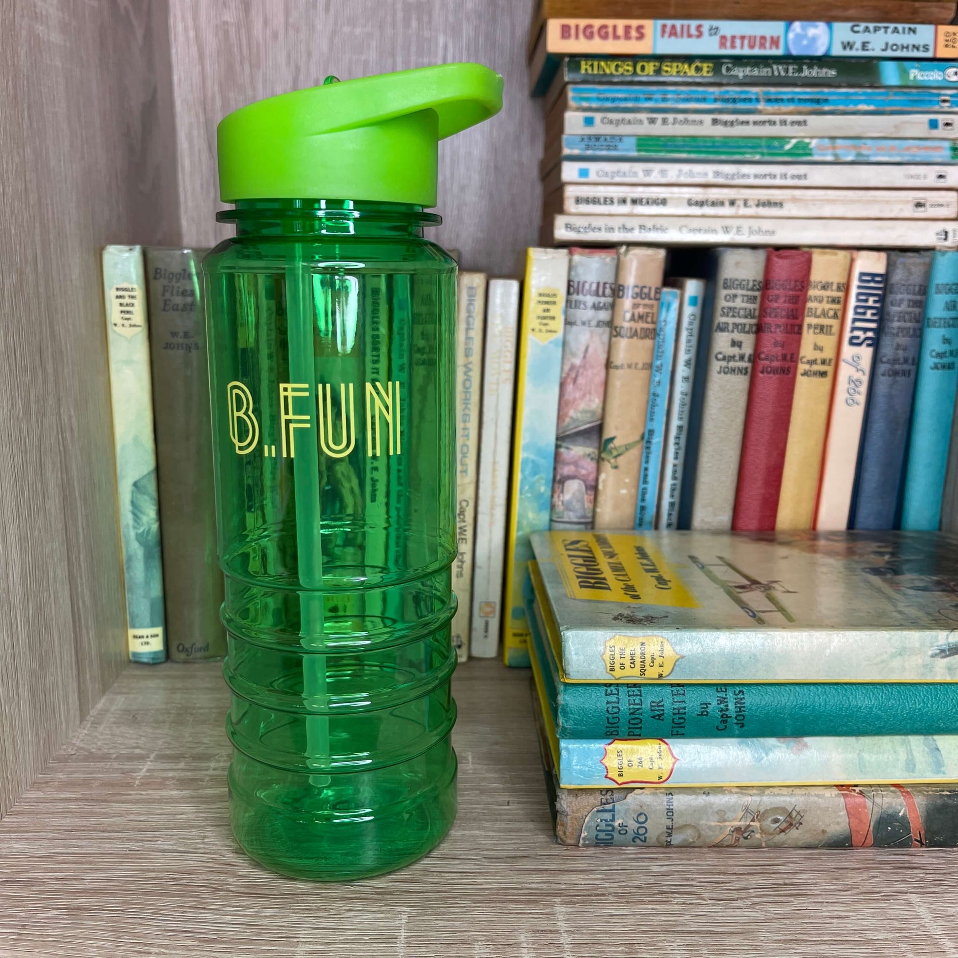 Bright green plastic sports water bottle with B=Fun printed on it sitting on a book shelf next to vintage books.