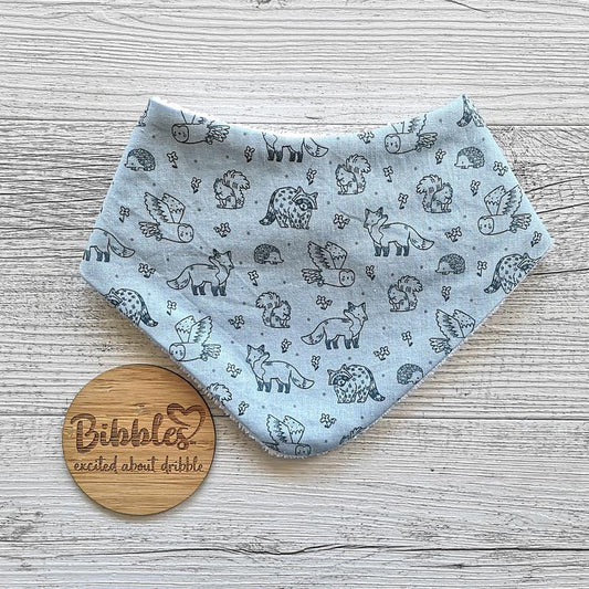 Baby dribble bib in light blue fabric with darker blue woodland animals printed on it.