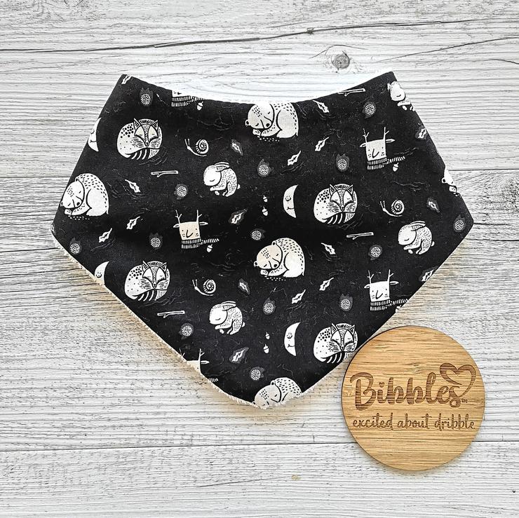 Baby dribble bib in black fabric with white sleeping bears, foxes and rabbits.