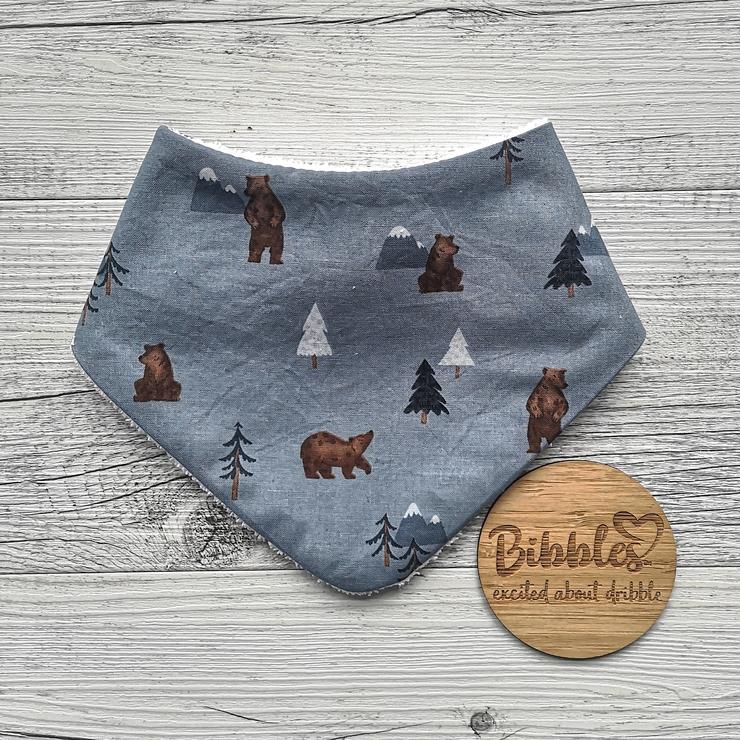 Baby dribble bib in dusky blue fabric with bears and pine trees printed on it.
