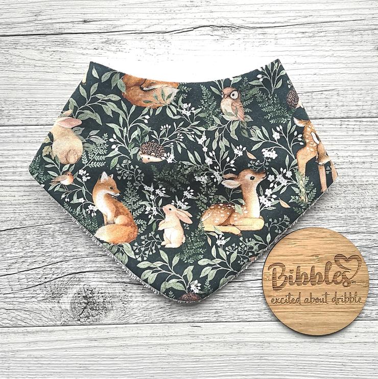 Baby dribble bib in a dark green fabric with deer, foxes, hedgehogs, owls, birds, rabbits and foliage.