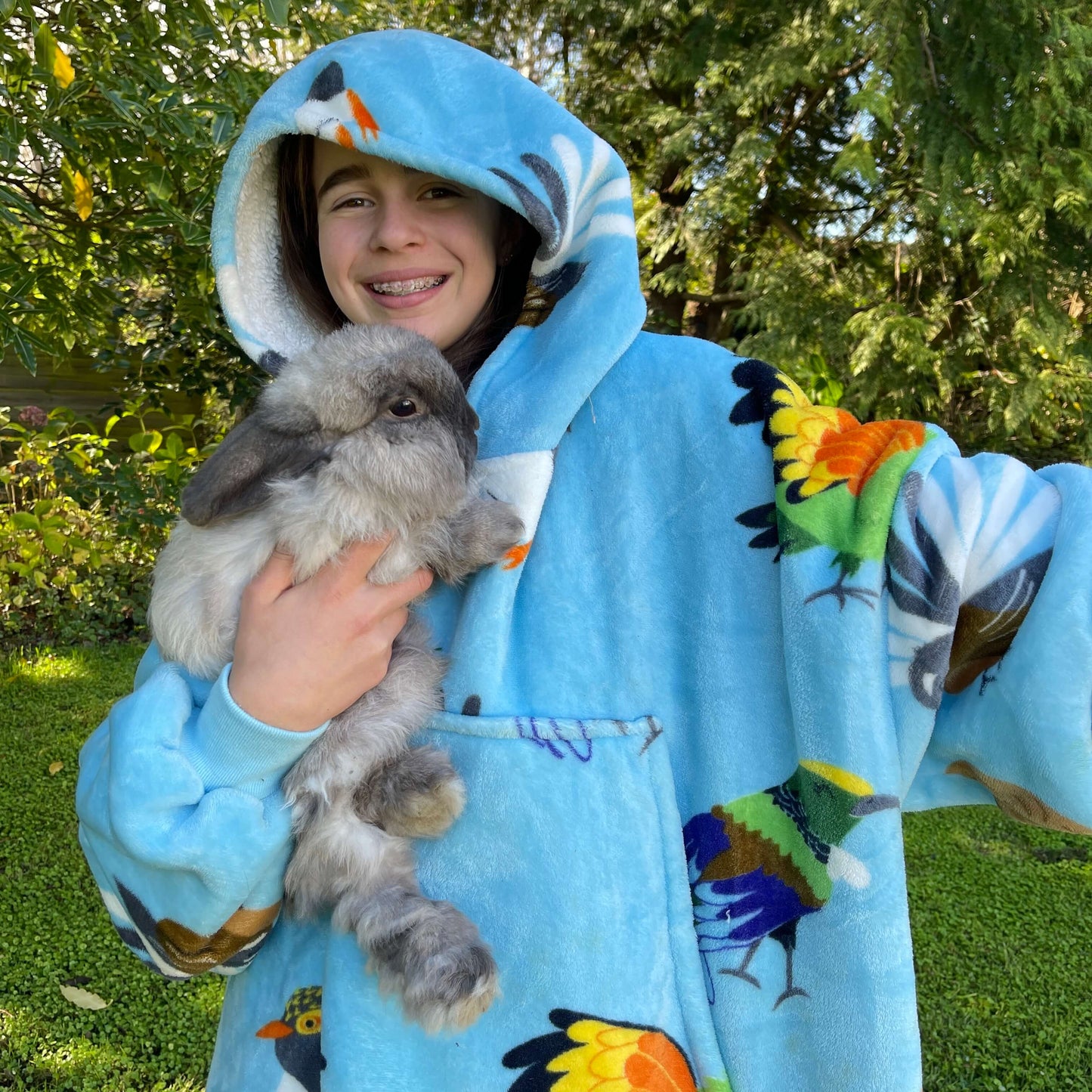 Young girl holding a bunny rabbit wearing an oversized blue hoodie with New Zealand birds printed on it.