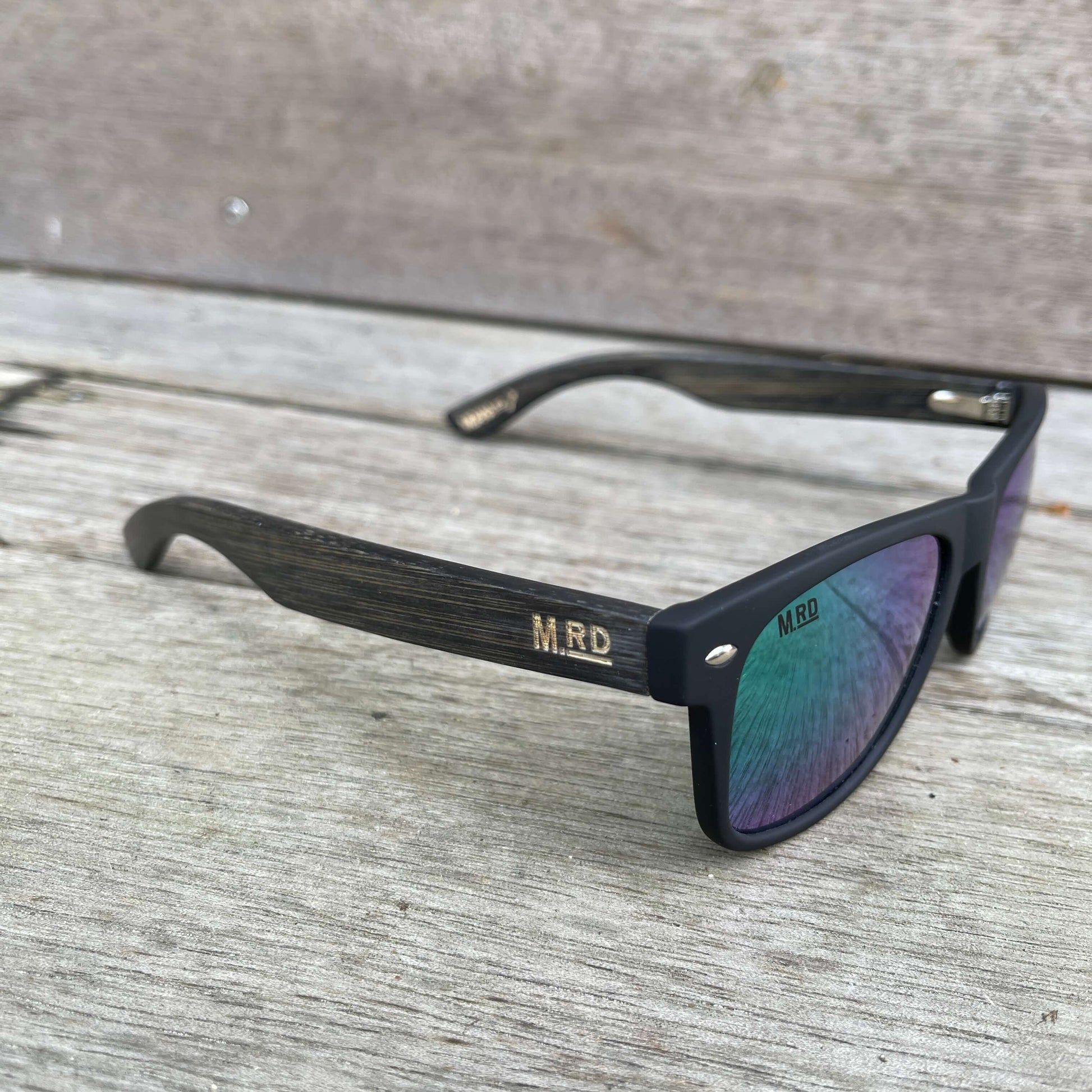 Sunglasses with dark wooden arms, black frames and green reflective lenses.
